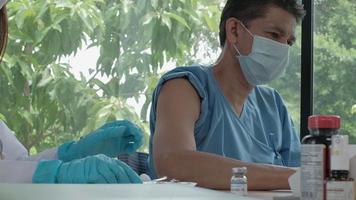 Doctora con mascarilla que vacuna a un paciente masculino, protege el coronavirus covid-19 en la clínica del hospital. Las inyecciones son el tratamiento de enfermedades, previenen la infección por enfermedades usando medicamentos saludables. video