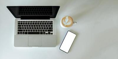 Vista superior simulacro de smartphone con ratón, ordenador portátil y taza de café. Espacio de copia plano. foto