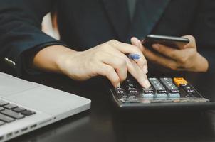 empresario sosteniendo una pluma y un teléfono para presionar una calculadora. negocios financieros, bancarios o tributarios y de inversión. foto