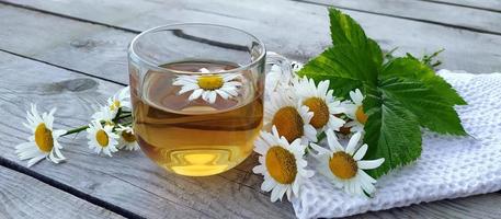 Chamomile aromatic tea in a glass cup on a wooden background. Floral banner. Summer still life with wildflowers and medicinal herbal drink, relaxation and detox. photo