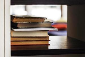 Many books stacked on black shelf with bokeh photo