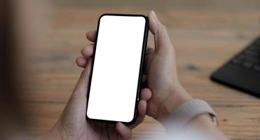 Mockup image blank white screen cell phone.women hand holding texting using mobile on desk at home office. photo