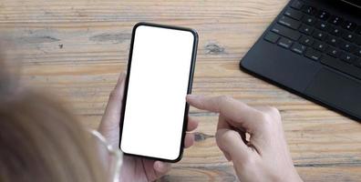 Mockup image blank white screen cell phone.women hand holding texting using mobile on desk at home office. photo