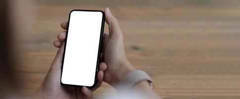 Imagen de maqueta en blanco teléfono celular con pantalla blanca. Mano de mujer sosteniendo mensajes de texto usando el móvil en el escritorio en la oficina en casa. foto