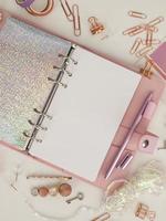 Diary opens with white and holographic page. Pink planner with cute stationery photographing in flatlay style. Top view of pink planner with business stationery. Pink glamour planner decoration photo