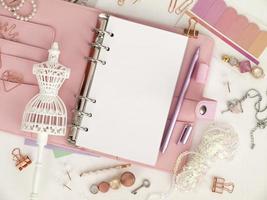 Top view of a pink planner with cute stationery. Pink glamour planner with a white mannequin figurine. Planner with open pages on a white background and with beautiful accessories pens, buttons, pins. photo