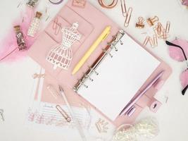 Top view of a pink planner with cute stationery. Pink glamour planner with a white mannequin figurine. Planner with open pages on a white background and with beautiful accessories pens, buttons, pins. photo