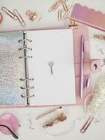 Silver key on the white page of the planner. Diary open with white and holographic page. Pink planner with cute stationery. Top view of the pink planner with stationery. photo