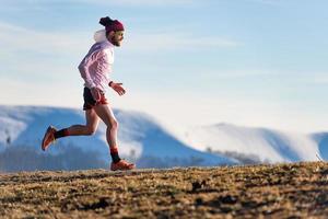 carrera de montaña. Entrenamiento de un atleta entre prados y nieve. foto