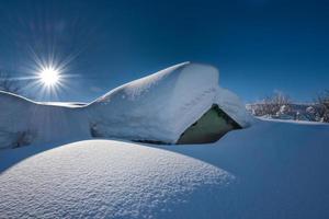 pequeña casa cubierta con mucha nieve después de fuertes nevadas foto