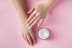 Female hands with a bottle of cream on pink background. Spa and body care concept. Image for advertising. photo