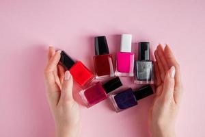 Female hands with bright nail polishes. A group of colored nail enamel on pink background.