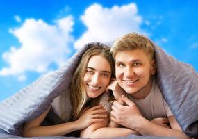 Happy beautiful couple in bed isolated on blue sky background, stay at home concept, coronavirus quarantine background, self isolation, life style at home photo