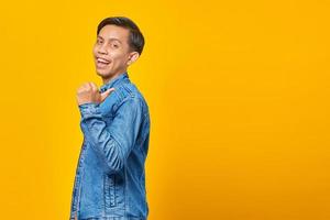 Handsome Asian man cheerful and pointing to empty space isolated on yellow background photo