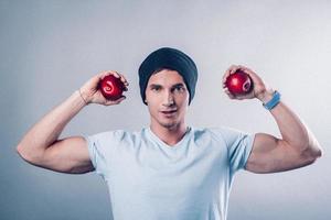Joven apariencia deportiva muestra músculos y sostiene manzanas en sus manos foto