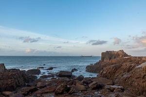 In the morning, the sun shines on the rocks and waves on the beach photo