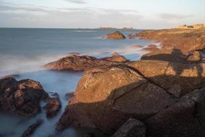 In the morning, the sun shines on the rocks and waves on the beach photo