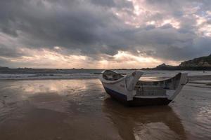 A small boat docked on the cloudy beach, and the sky was covered with dark clouds photo