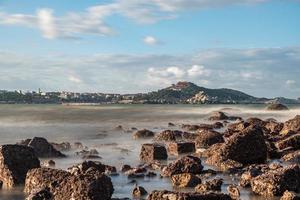 In the morning, the sun shines on the rocks and waves on the beach photo