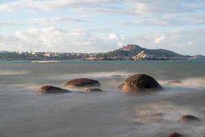 In the morning, the sun shines on the rocks and waves on the beach photo