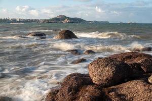 In the morning, the sun shines on the rocks and waves on the beach photo