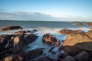 In the morning, the sun shines on the rocks and waves on the beach photo