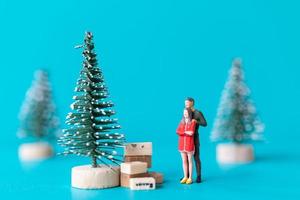 Gente en miniatura, pareja de enamorados de pie junto a un árbol de navidad foto