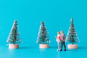 Gente en miniatura, pareja de enamorados de pie junto a un árbol de navidad foto