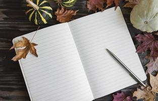 Pumpkins and leaves  frame with notebook on wooden background. photo