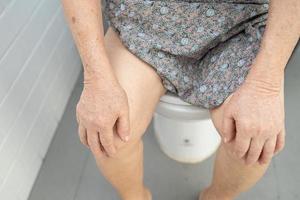 Asian senior or elderly old lady woman patient sitting on flush toilet in bathroom. photo