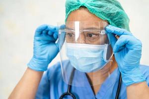 médico asiático con protector facial y traje de ppe nuevo normal para comprobar que el paciente protege la seguridad infección brote de coronavirus covid-19 en la sala de cuarentena del hospital de enfermería. foto