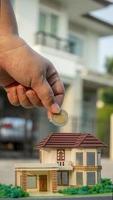 Mano poniendo moneda de dinero en el modelo de la casa para las finanzas comerciales y el concepto de préstamo hipotecario. foto