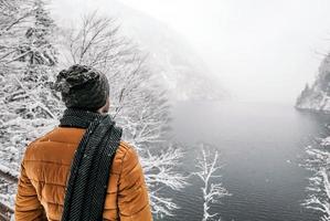 Vista posterior de un hombre en ropa de invierno disfrutando del invierno brumoso cerca de un río de montaña foto