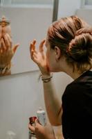 Primer plano vertical de una mujer poniéndose crema facial en el espejo del baño