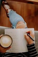 Vertical shot of a lady holding coffee and filling in a journal