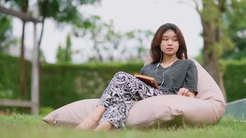 A beautiful Asian woman enjoys listening to music with earphones with feeling happy and relaxed in the outdoors in her home garden.