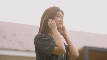 een mooie aziatische vrouw luistert graag naar muziek met oortelefoons en voelt zich gelukkig en ontspannen in de buitenlucht in haar eigen tuin. video