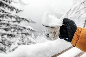 Primer plano de una mano en guantes de invierno sosteniendo una taza llena de nieve foto