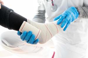 Unrecognizable doctor bandaging leg of elderly patient photo