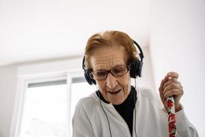 Delighted senior woman listening to music and doing housework photo