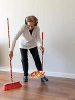Sonriente anciana limpiando el piso y escuchando música. foto