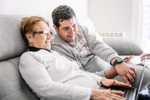 Cheerful man and senior woman using laptop together photo