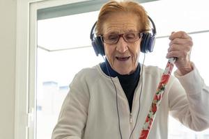 Delighted senior woman listening to music and doing housework photo