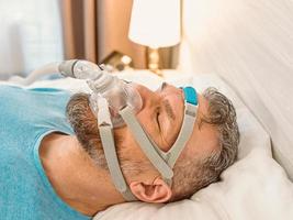 El hombre dormido con problemas respiratorios crónicos considera usar una máquina cpap en la cama. cuidado de la salud, terapia de apnea obstructiva del sueño, cpap, concepto de ronquidos foto