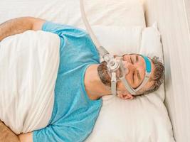 Sleeping man with chronic breathing issues considers using CPAP machine in bed. Healthcare, Obstructive sleep apnea therapy, CPAP, snoring concept photo