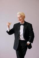 stylish mature sommelier senior woman in tuxedo with glass of sparkling wine. Fun, party, style, lifestyle, alcohol, celebration concept photo