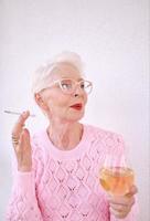 Old fashioned senior stylish woman smoking cigarette with glass of white wine. Bad habit, addiction concept