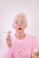 antigua mujer con estilo senior fumando cigarrillos con una copa de vino blanco. mal hábito, concepto de adicción foto