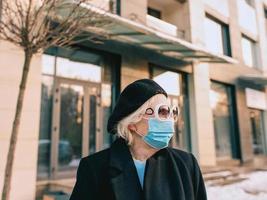 senior stylish woman in beret and elegant black coat and in medical mask walking outdoor. Lockdown, pandemic, protection concept photo