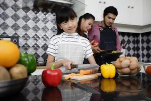familia feliz tiene a papá, mamá y su pequeña hija cocinando juntos en la cocina foto